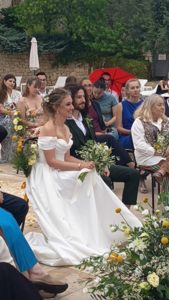Meitar e Aliénor seduti durante la cerimonia nuziale in Sicilia, rivolti verso il celebrante.