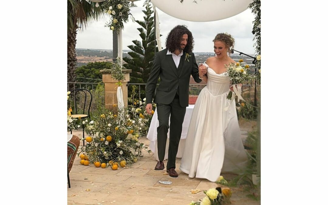 Meitar e Aliénor davanti alla chuppah decorata con fiori, limoni e rami d’ulivo durante la cerimonia in Sicilia.